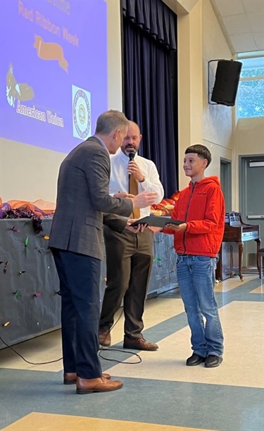 Assistant District Attorney Jerry Stanley attends Red Ribbon Week at a local elementary school, presenting awards to students and engaging in meaningful conversations about drug prevention and healthy choices. His presence and support makes a positive impact on the young minds in the community.